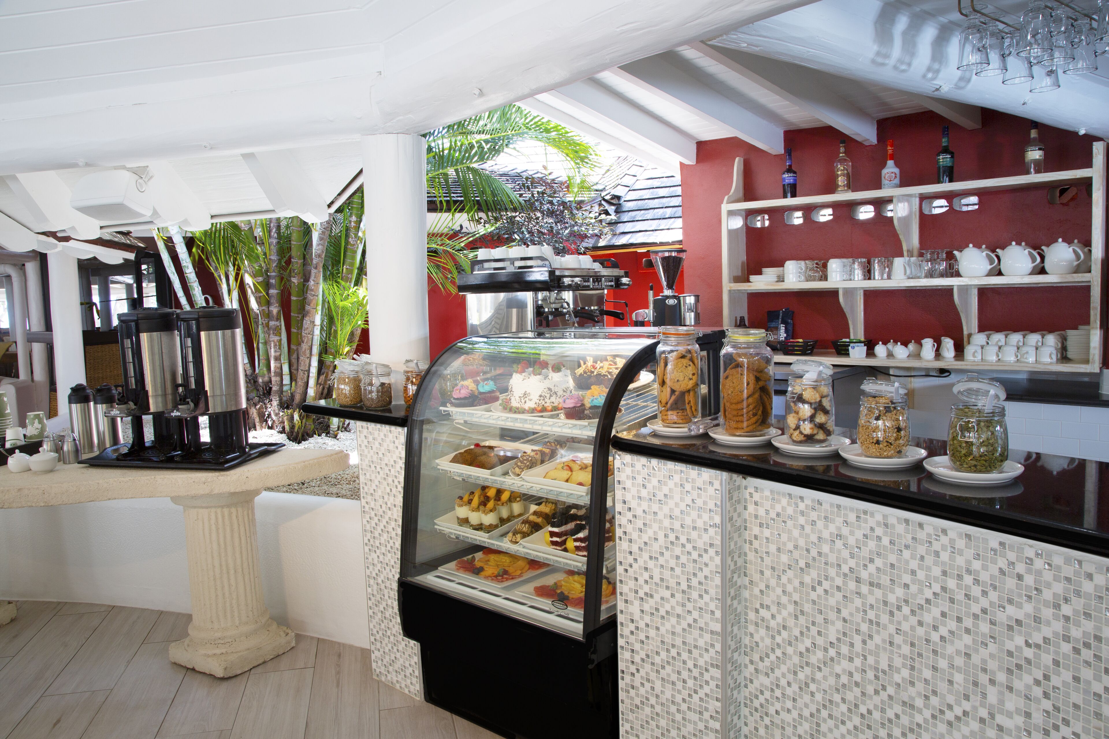 Une vitrine de pâtisserie présentant divers gâteaux et une station où l'on peut se servir du café.