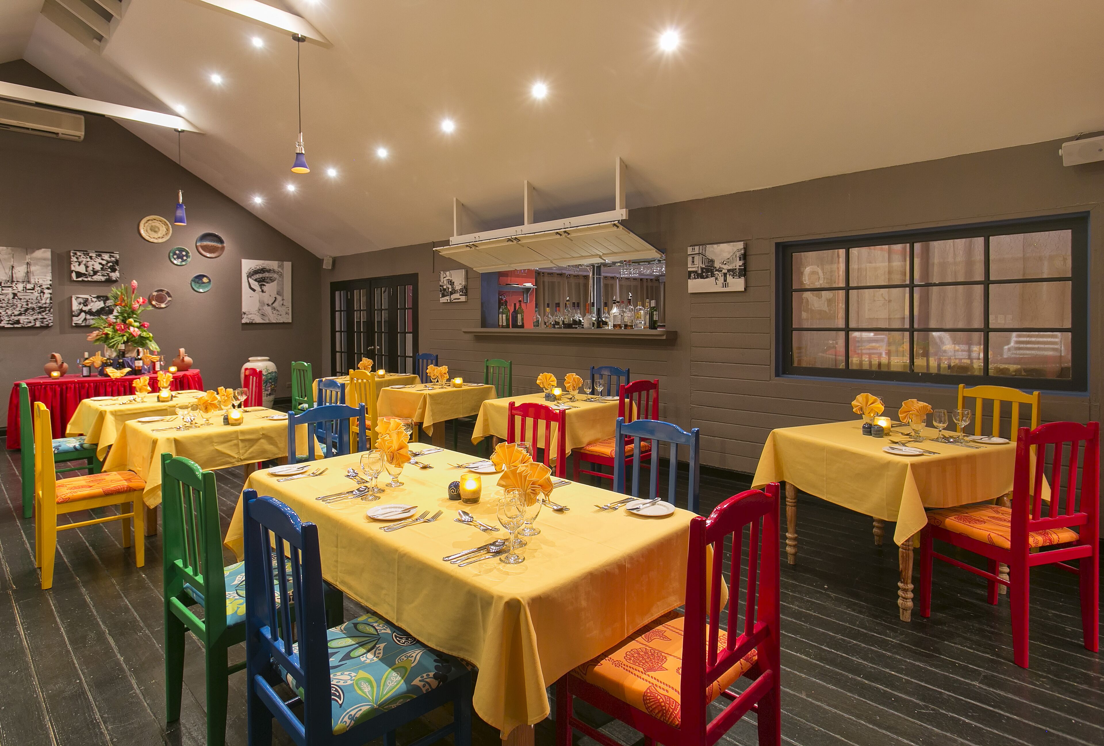 Una sala ristorante con diversi tavoli apparecchiati, sedie colorate e tovaglie gialle.