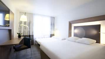 A hotel room with a large bed, a desk with a chair, a potted plant, and a window with curtains.