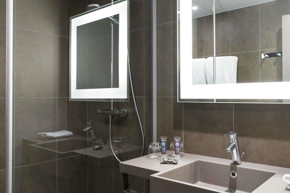 A modern bathroom with a large mirror, a shower, and a sink with toiletries.