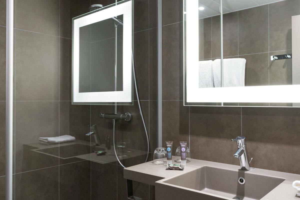 A modern bathroom with a large mirror, a shower, and a sink with toiletries.