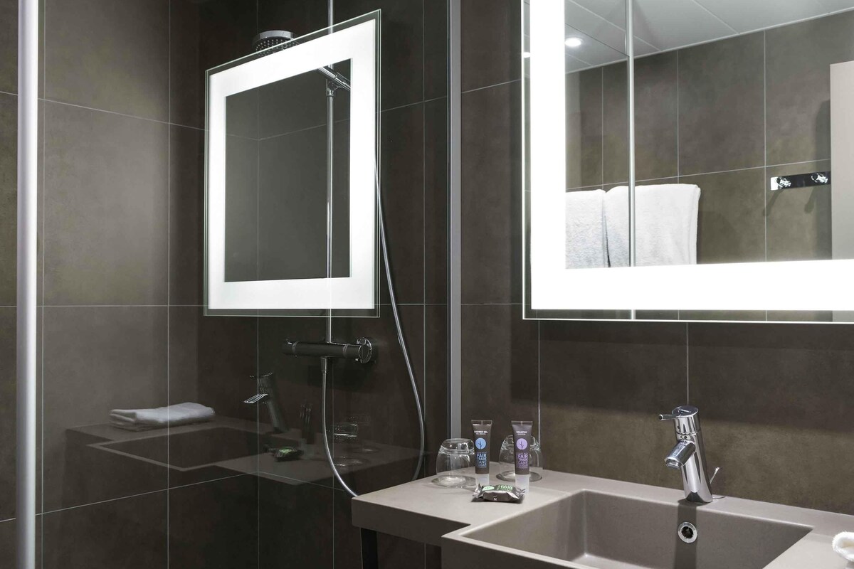 Un baño moderno con un espejo grande, ducha, lavamanos y toallero.
