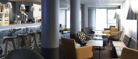 Un espacio lounge moderno con techos altos, pilares grandes y mobiliario contemporáneo.