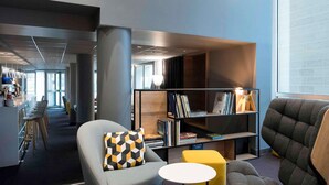 A modern library with a grey armchair, a yellow ottoman, and a bookshelf filled with books.