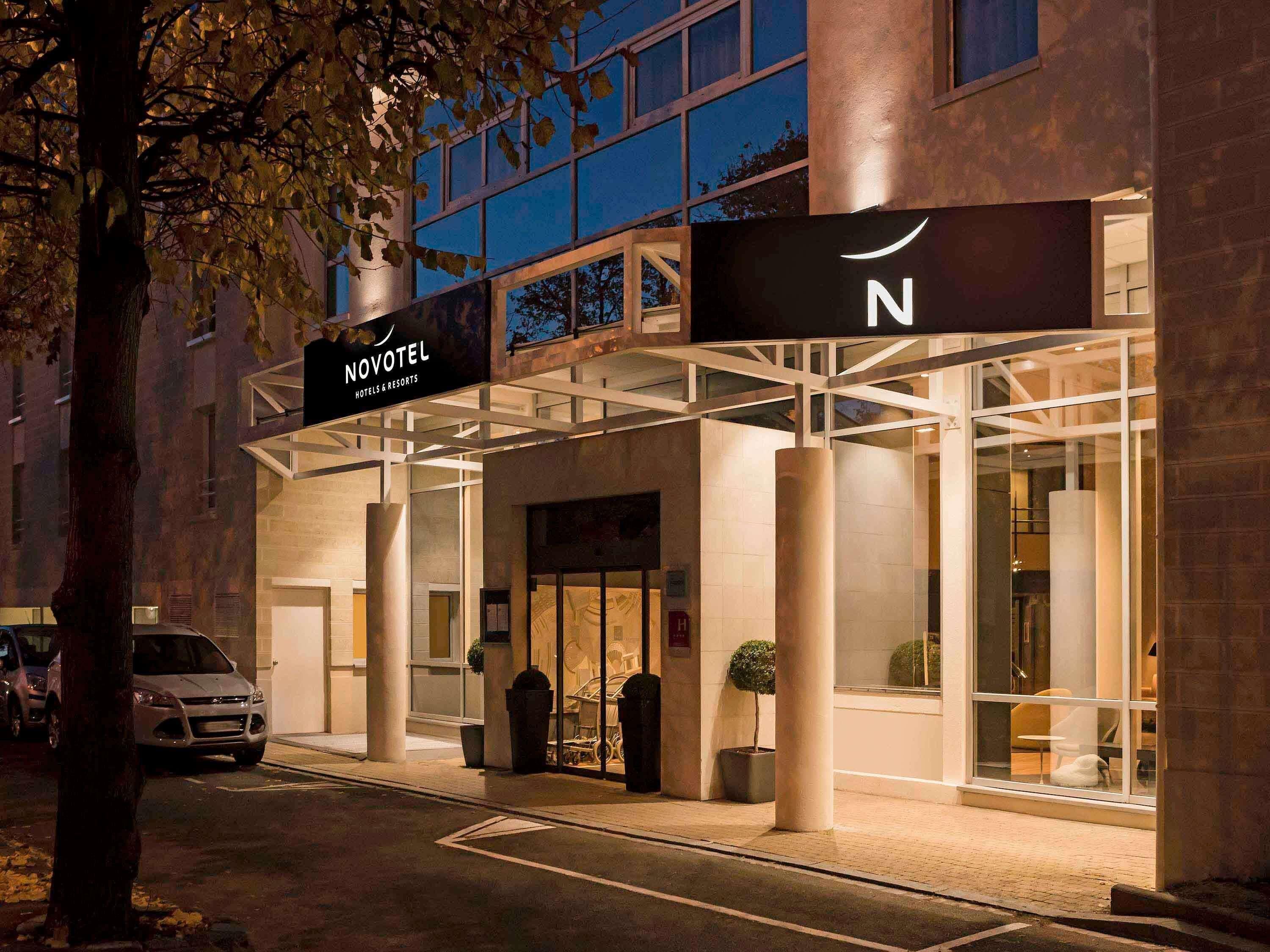Fachada de hotel de diseño moderno, con un llamativo letrero 'NOVOTEL', grandes columnas y un frente de vidrio.