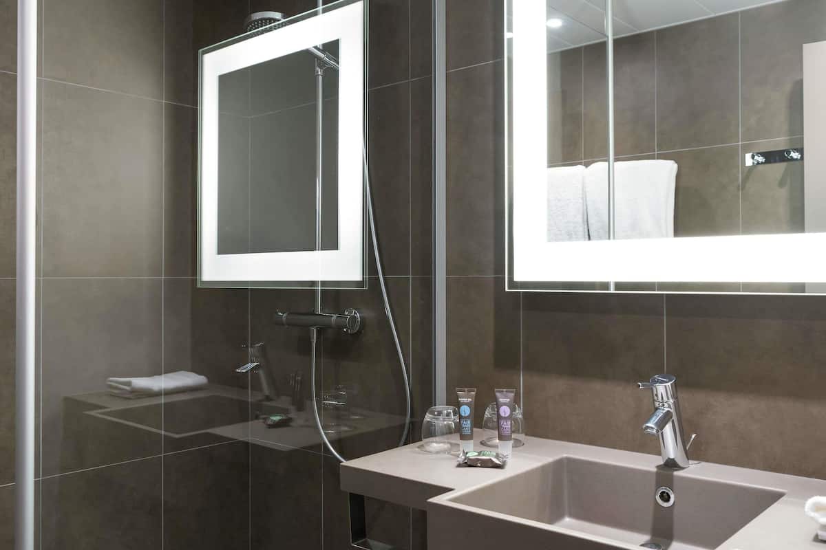 A modern bathroom with a large mirror, a shower, and a sink with toiletries.