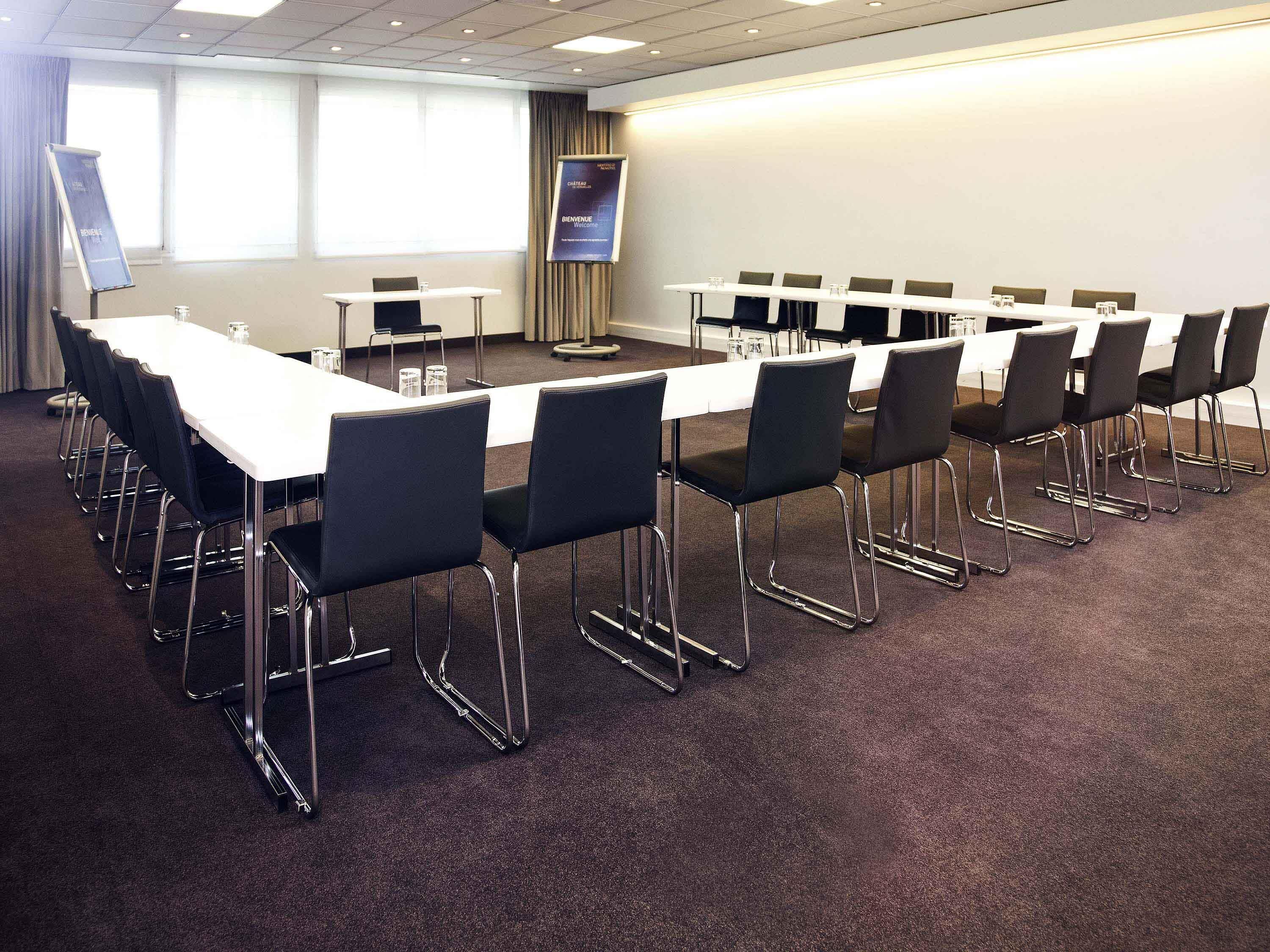 Une salle de conférence avec une longue table, des chaises noires et un écran de projection.