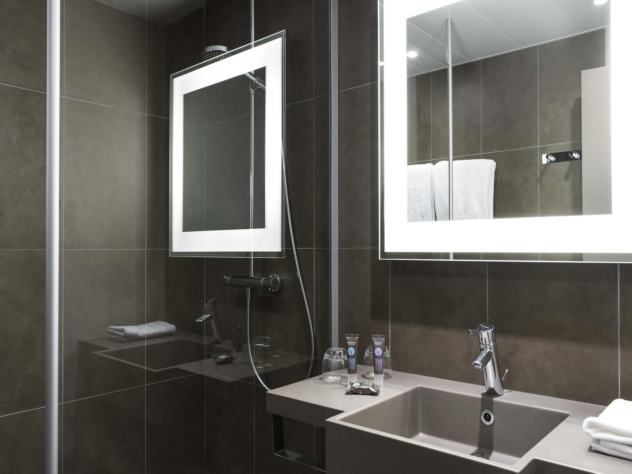 A modern bathroom with a glass shower enclosure, a large mirror, a sink with a faucet, and toiletries on the countertop.