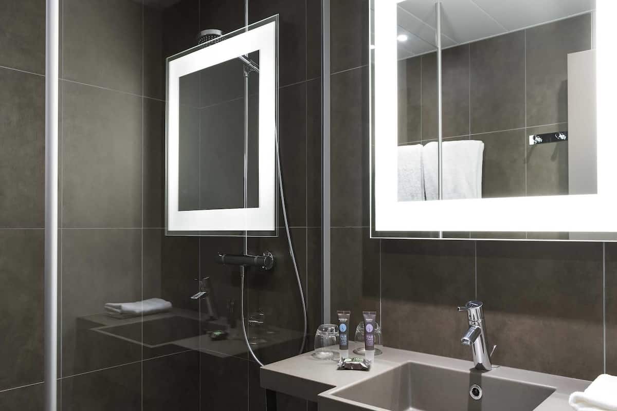 A modern bathroom with a glass shower enclosure, a large mirror, a sink with a faucet, and toiletries on the countertop.