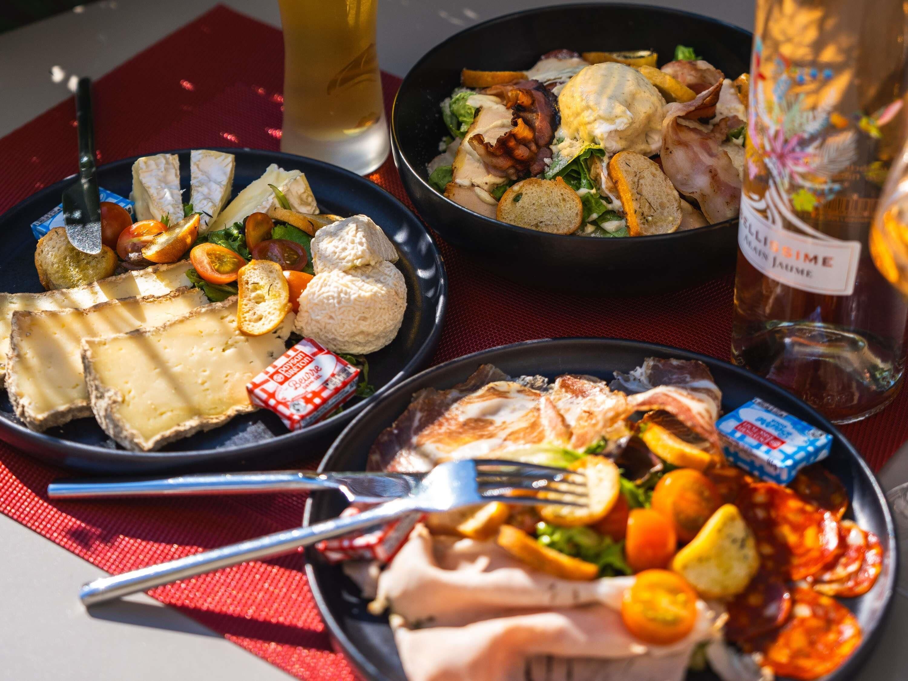 A table with various dishes including cheese, bread, and a salad, along with a bottle of wine.