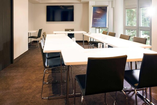 A conference room with a long table, chairs, a projector screen, and a welcome screen.