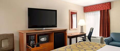 A hotel room with a bed, a television, a desk with a lamp, a chair, and a safe.