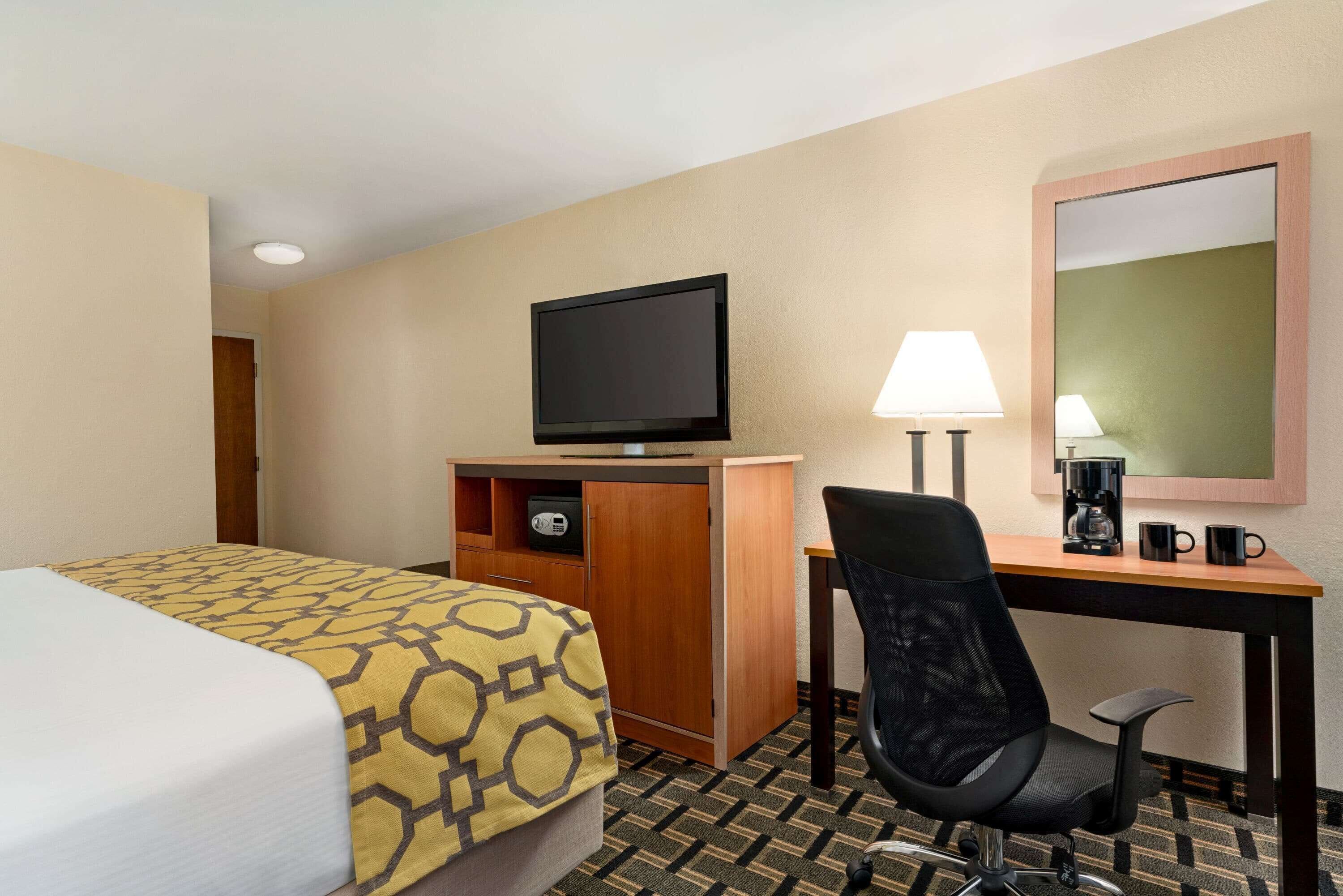 A hotel room with a bed, a desk, a chair, a television, a lamp, and a coffee maker.