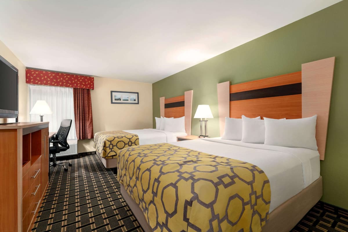 A hotel room with two beds, a desk, a chair, and a TV.
