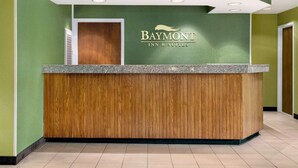Un mostrador de recepción con diseño de panel de madera, una pared verde con el logotipo de Baymont Inn & Suites y un techo blanco con iluminación empotrada.