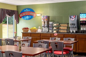 Rincón de desayuno con un letrero que dice "Baymont Breakfast Corner", una máquina de café, un dispensador de bebidas y una bandeja de pasteles.