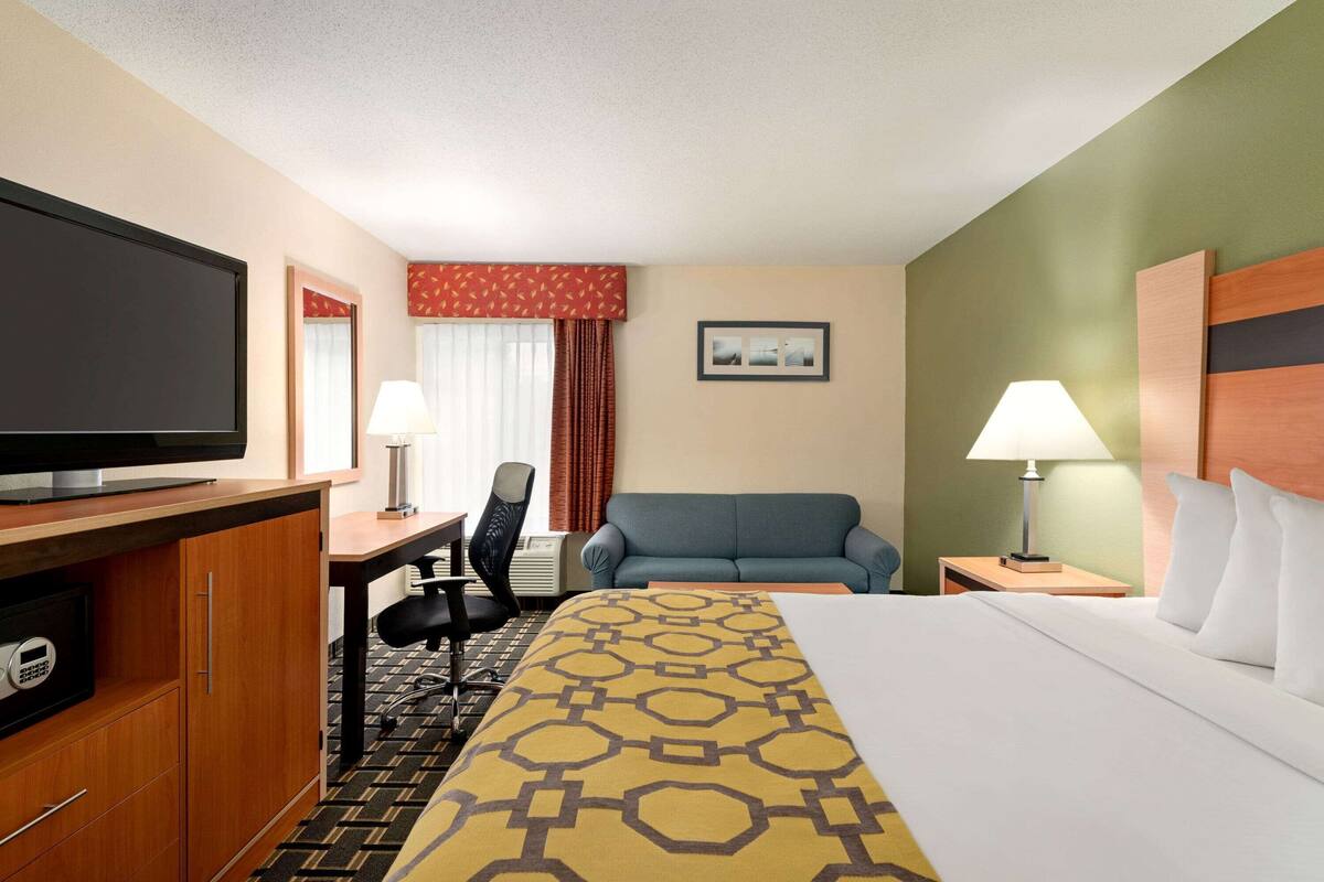 A hotel room with a bed, a desk, a television, a chair, and a nightstand with a lamp.