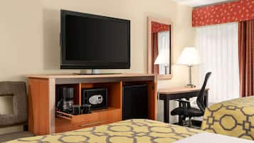 A hotel room with a bed, a desk, a chair, a television, a coffee maker, a safe, and a mirror.