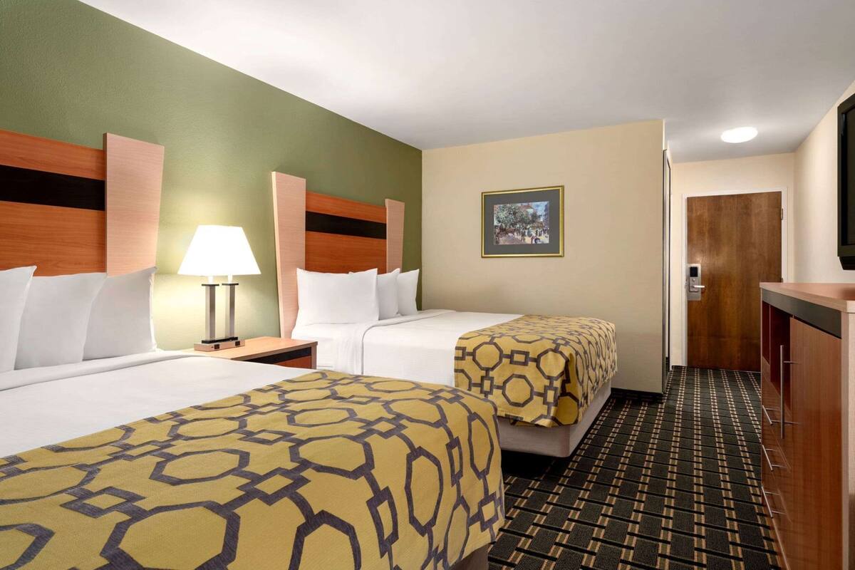 A hotel room with two beds, a bedside table with a lamp, a framed picture on the wall, and a patterned carpet.