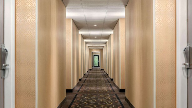 Un largo y estrecho pasillo de hotel con alfombra estampada y paredes color beige.