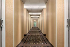 A long, narrow hotel corridor with patterned carpet and beige walls.