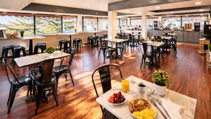 Un comedor amplio con varias mesas y sillas, una cocina al fondo y grandes ventanales con vistas.