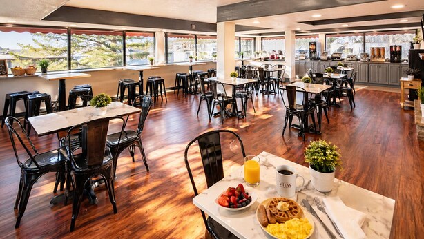 A spacious dining area with multiple tables and chairs, a kitchen in the background, and large windows offering a view. - The View Inn & Suites (Bethlehem)