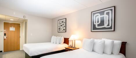 A hotel room with two beds, a nightstand with a lamp, and two framed abstract artworks on the wall.