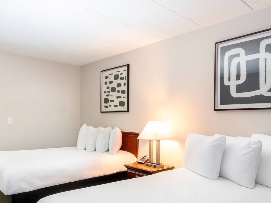 Une chambre d’hôtel avec deux lits, une table de chevet avec une lampe et deux œuvres d’art abstraites encadrées accrochées au mur.