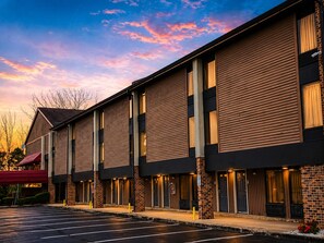 A hotel with a row of rooms, a parking lot, and a clear sky.