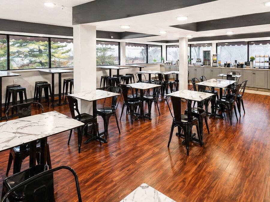Un restaurante con mesas de mármol y sillas negras, un área de cocina y amplios ventanales con vistas.