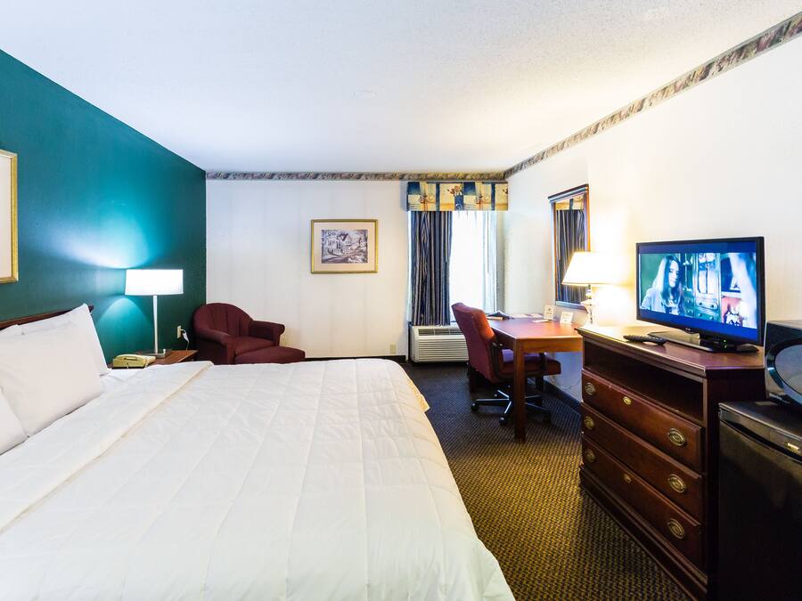 A hotel room with a large bed, a desk with a chair, a television, and a dresser.