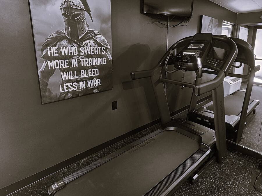 A treadmill in a gym with a motivational poster on the wall.