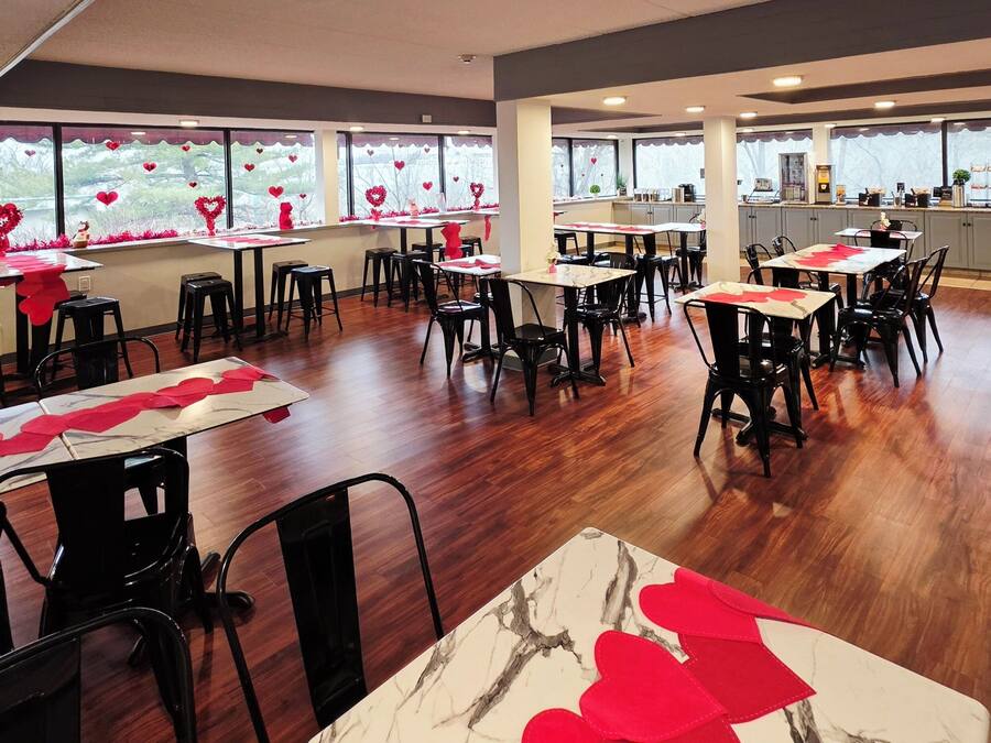 A restaurant with multiple tables and chairs, large windows with heart decorations, and a kitchen area visible in the background.