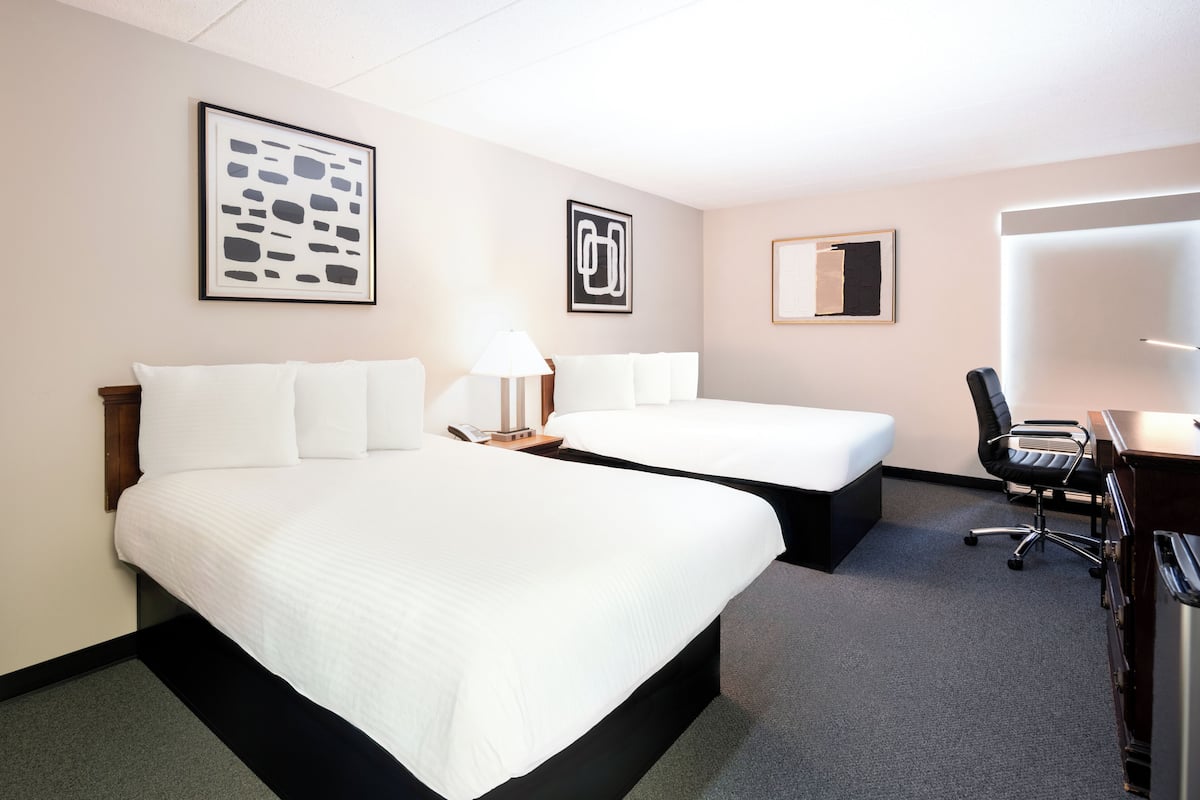 A hotel room with two beds, a desk, a chair, and artwork on the walls.