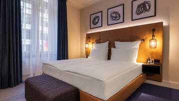 A hotel room with a large bed, a nightstand, three framed artworks, and a window with curtains.