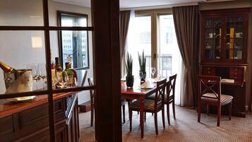 Une salle à manger d’hôtel avec une table en bois dressée pour quatre personnes, un buffet avec des portes en verre et une vue sur la ville à travers de grandes fenêtres.