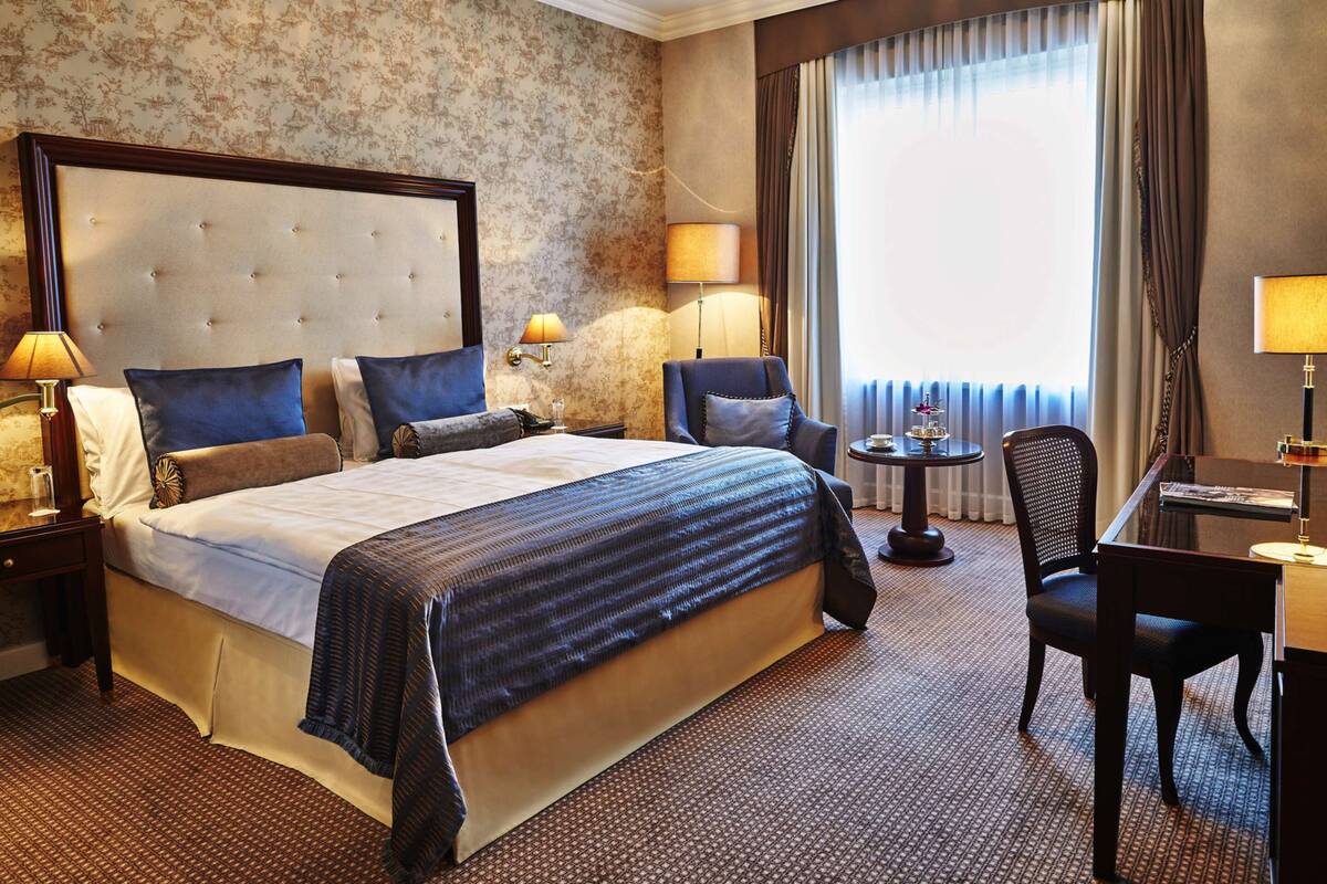 Ein Hotelzimmer mit einem großen Bett, zwei Stühlen, einem kleinen Tisch und einem Schreibtisch.