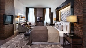 Ein modernes Hotelzimmer mit einem großen Bett, einem Schreibtisch, einem Sessel, einem Fernseher und einem Wand-Fernseher.