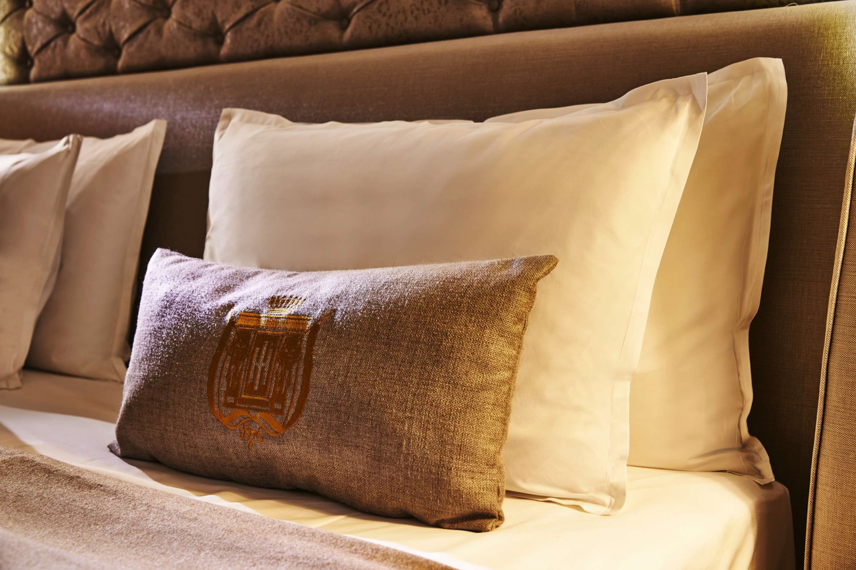 Una cama con almohadas blancas y marrones, una con un logotipo.