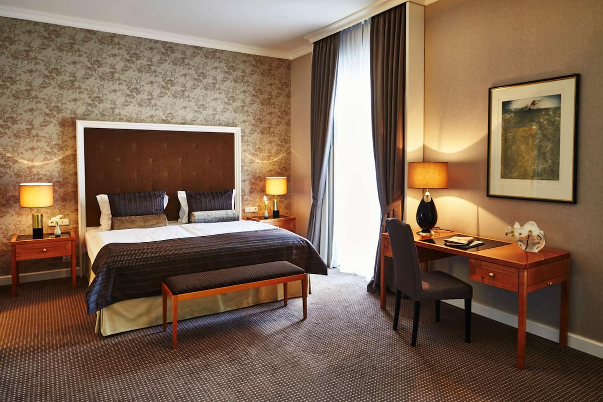 Ein Hotelzimmer mit einem großen Bett, zwei Nachttischen mit Lampen, einem Schreibtisch mit Stuhl und einem gerahmten Bild an der Wand.