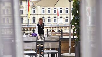 An outdoor dining area with a table set for two, a waiter, and a view of a historic building in the background.