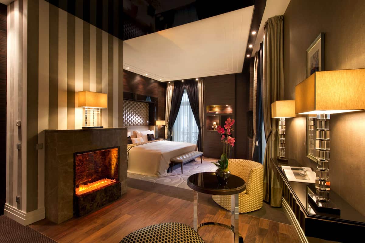 Ein modernes Hotelzimmer mit Kamin, einem Bett, einer Sitzecke mit Tisch und einem großen Fenster mit Vorhängen.