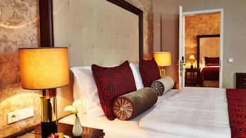 A hotel room with a large bed, a nightstand with a lamp, a vase with flowers, and a plate of fruit.