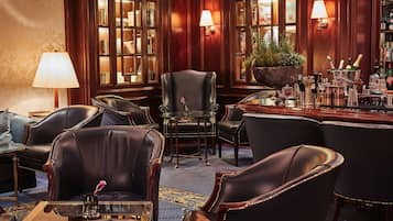 A bar area with leather chairs, a bar counter with bottles, and a large potted plant.