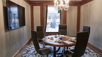 A conference room with a round table, six chairs, a chandelier, and a large window with a view of a building.