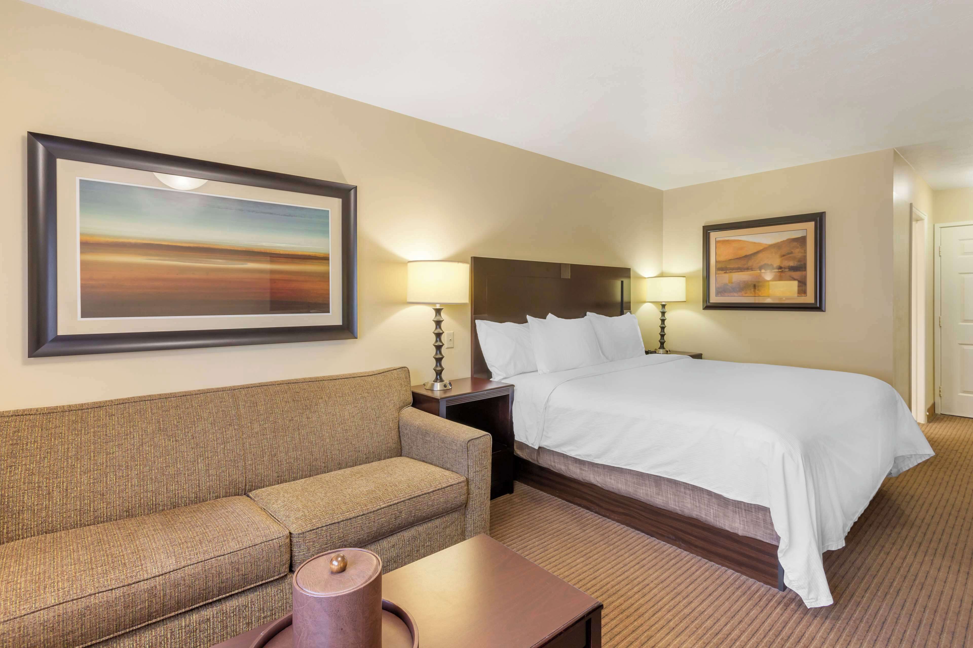 A hotel room with a bed, a sofa, two lamps, and two framed pictures on the walls.