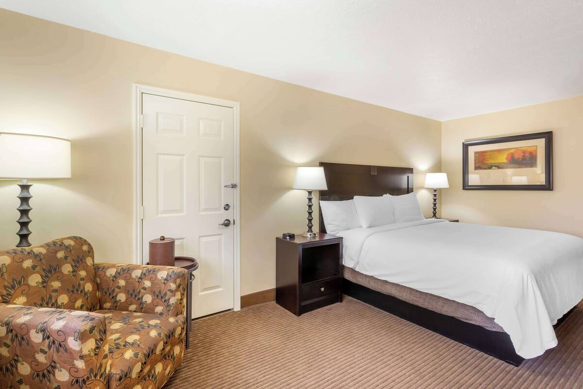Une chambre d’hôtel avec un lit, une chaise, une table de chevet et une porte.