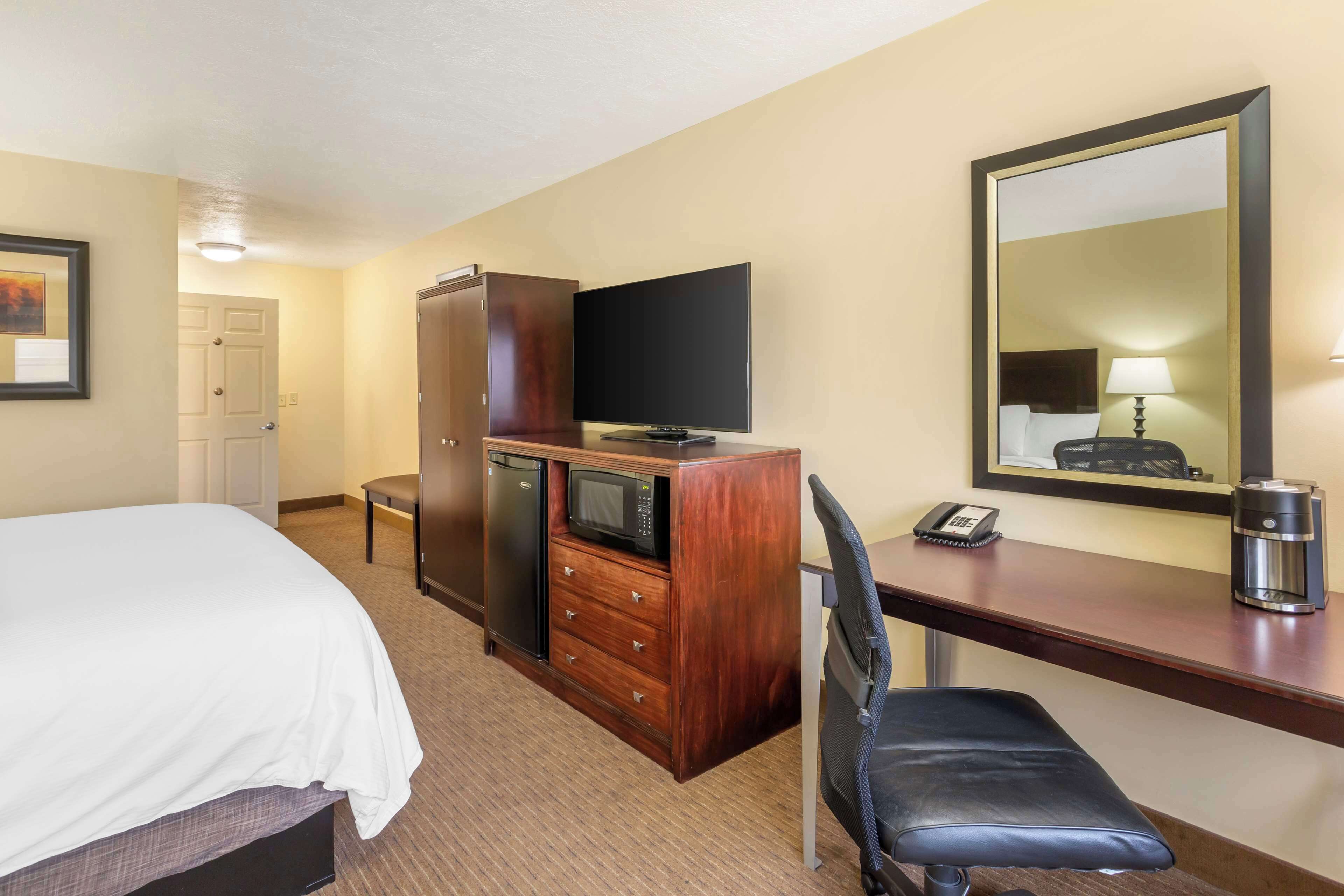 Une chambre d’hôtel comprenant un lit, un bureau avec une chaise, une télévision, un four à micro-ondes, une machine à café et un miroir.