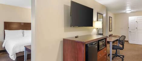A hotel room with a bed, a desk with a chair, a television, a refrigerator, and a dresser.